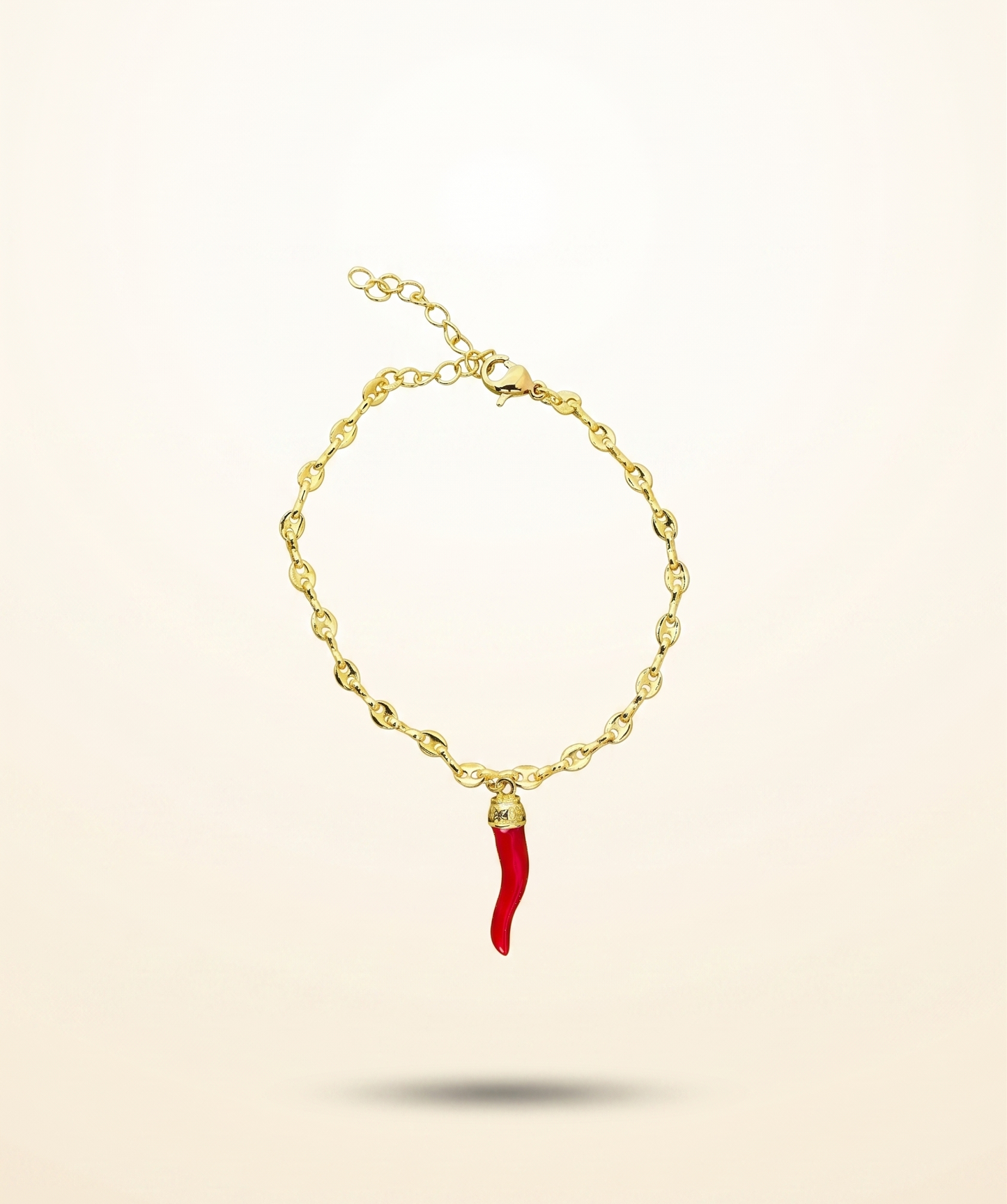 Gold bracelet with a red charm on a beige background