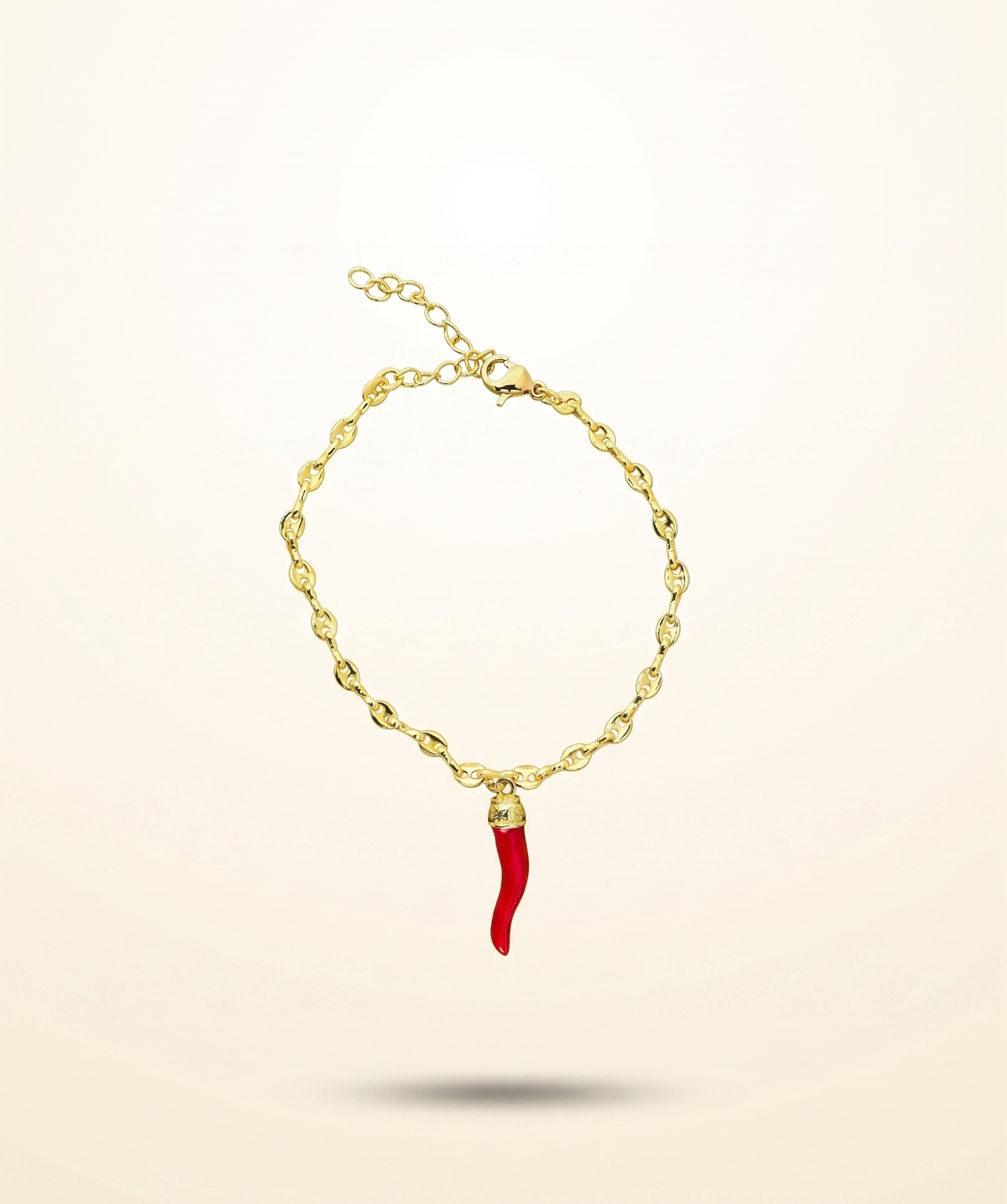 Gold bracelet with a red charm on a beige background